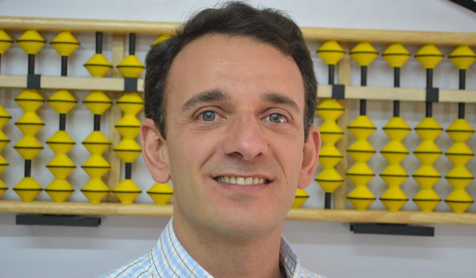 Juan José Chamie sonriendo frente a un Soroban grande de cuentas amarillas
